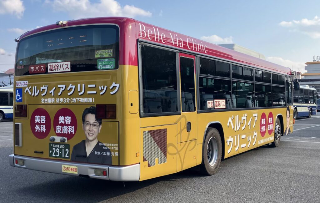 名古屋市の基幹バスに掲出されたベルヴィアクリニックのラッピング広告。加藤秀輝院長の肖像と、名古屋駅徒歩3分（地下街直結）の案内、美容外科・美容皮膚科の文字がデザインされています。