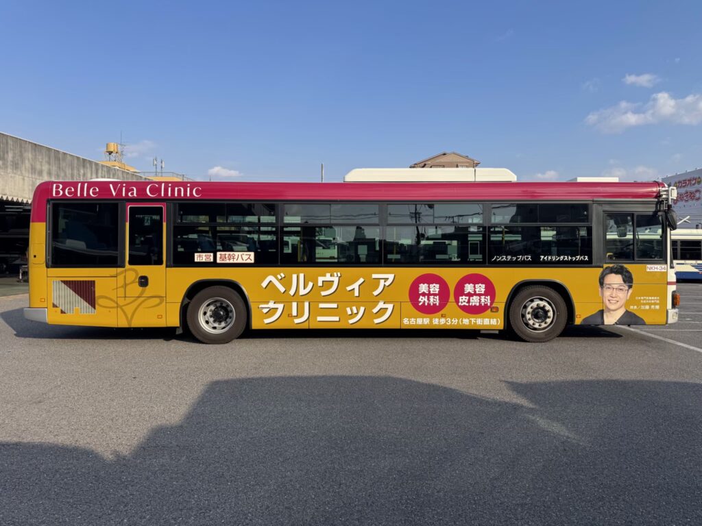 名古屋市内を走るベルヴィアクリニックのラッピングバス広告。形成外科専門医である加藤 秀輝院長の肖像とともに、美容外科・美容皮膚科の案内、名古屋駅徒歩3分（地下街直結）の文字が記載された車体側面のデザインです。
